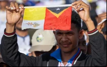 Joven de Timor Oriental levanta la bandera del Vaticano junto a la de su país en la Misa del Papa Francisco en Taci Tolu